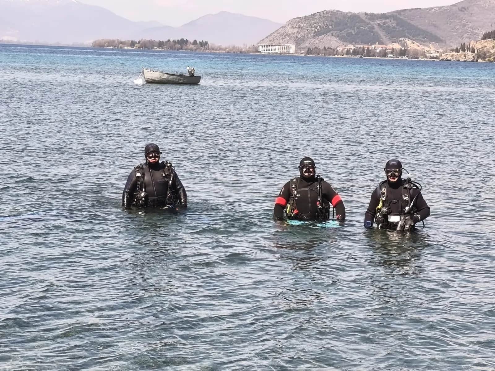 Тројца нуркачи на Amphibia излегуваат од водата кај плажата Дивоно, во заднина се планините над Охридското Езеро