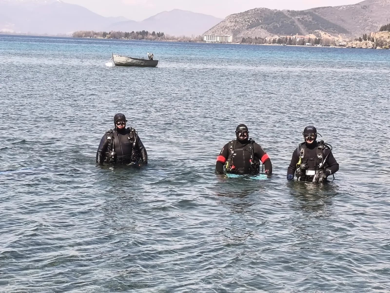 Three Amphibia scuba divers emerging from Lake Ohrid at Kaj Divono beach, mountains in the background