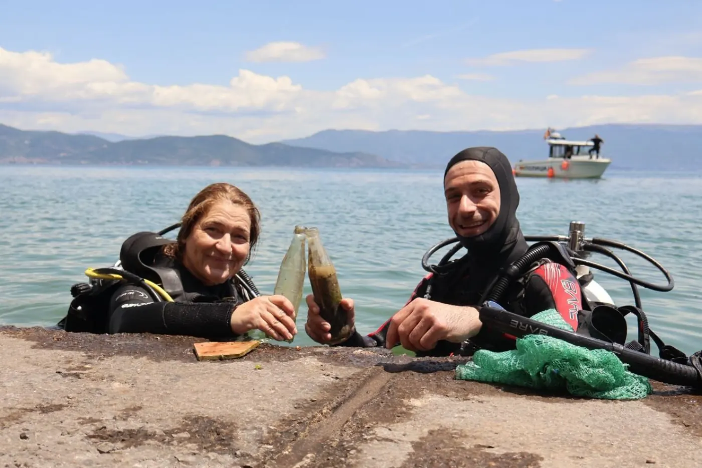 Two smiling scuba divers showing old glass bottles recovered from the bottom of Lake Ohrid